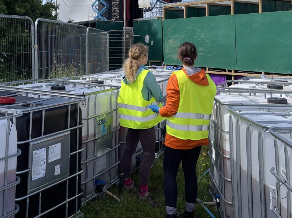 two women stand behind compost toliets, collecting urine